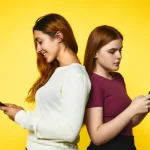 two-young-girls-stand-back-back-look-their-phones-standing